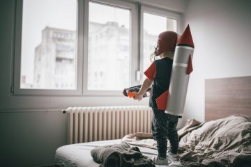 Ung gutt stående på senga med romrakett og leke pistol