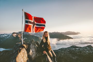 Dame på toppen av et fjell med det norske flagget