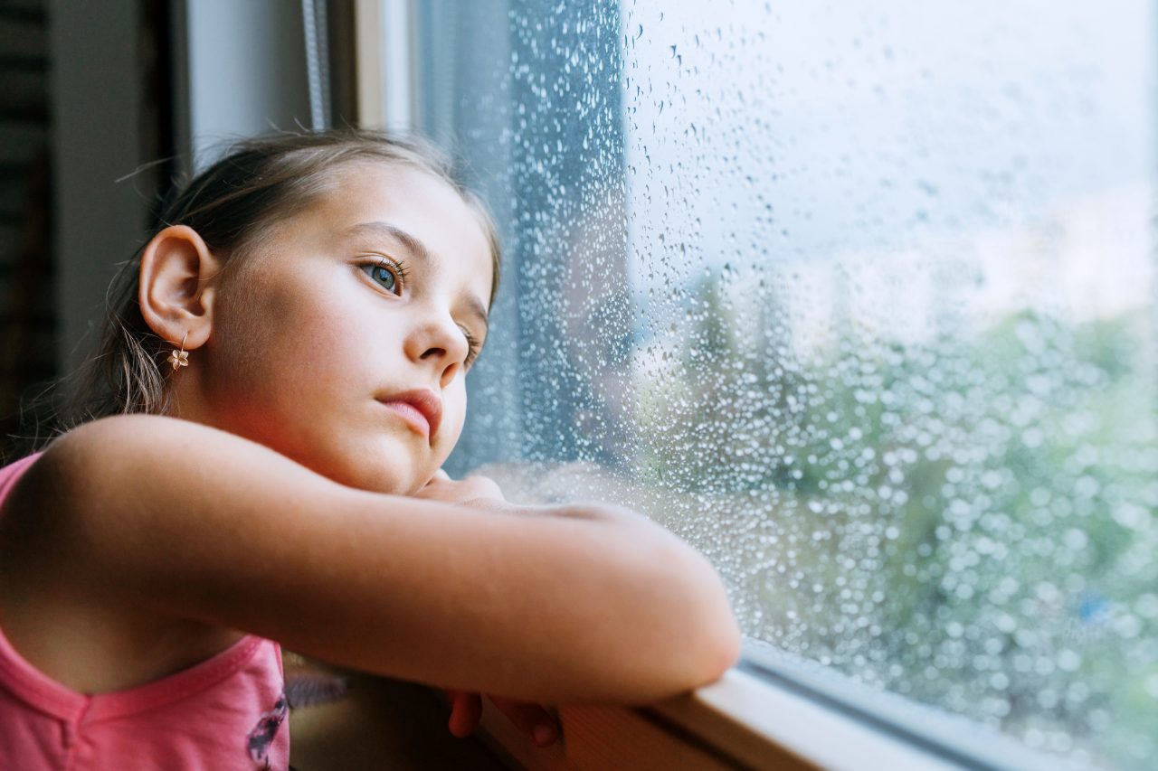 Liten jente ser tenkende ut av vinduet med regndråper på