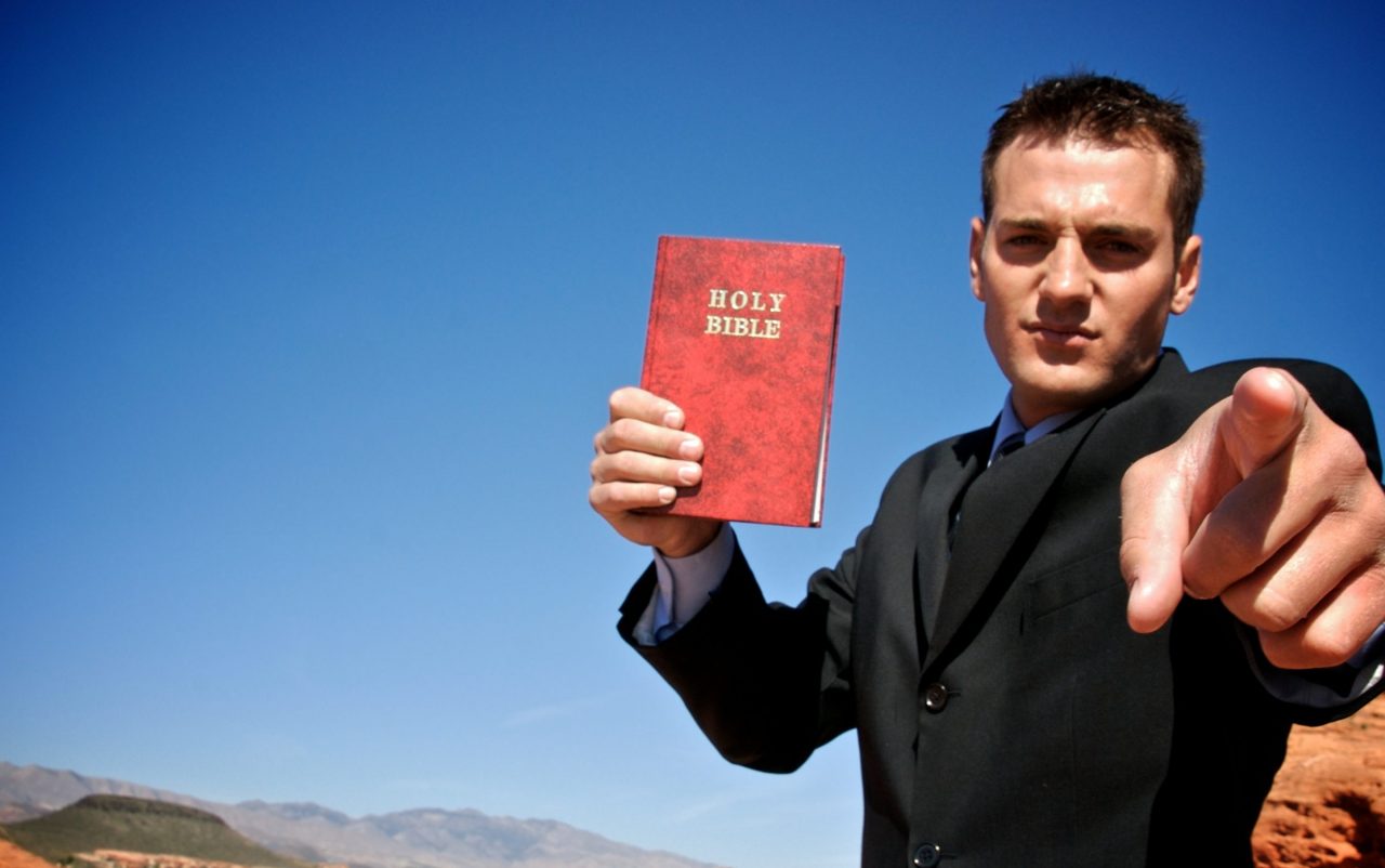 Mann peker og holder opp en bibel