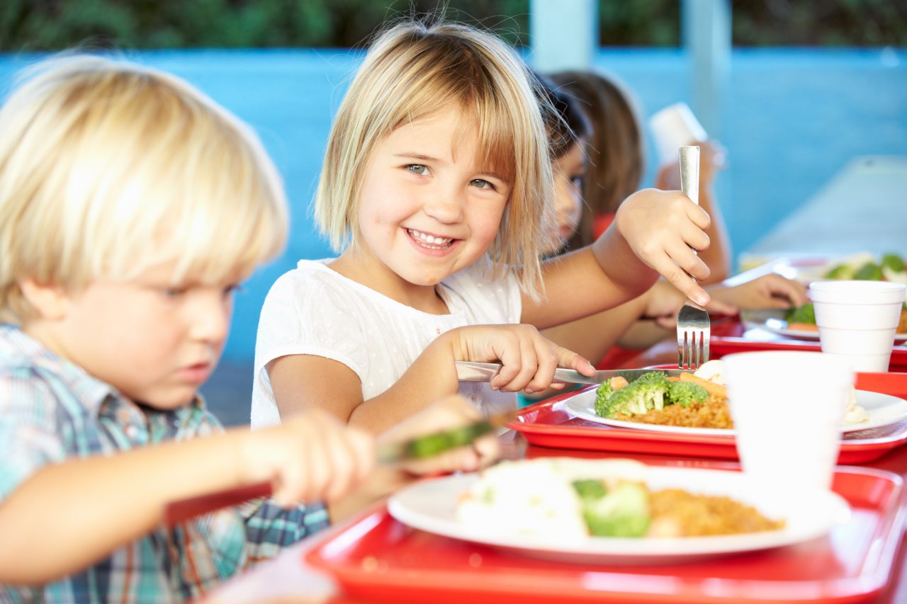 Fornøyde skolebarn i kantine spiser varmmat.