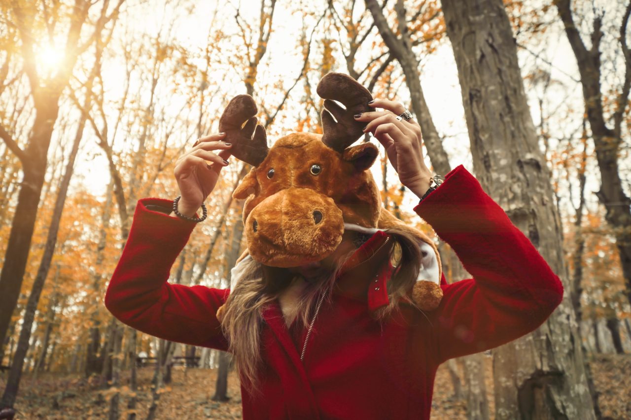 Kvinne i skogen, med elgmaske holder på geviet i stoff.