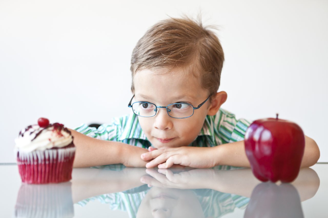 En liten gutt som skal bestemme seg for et eple, eller en cupcake