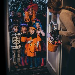 En dame åpner døra for en gjeng med barn og voksne som går knask eller knep på Halloween.