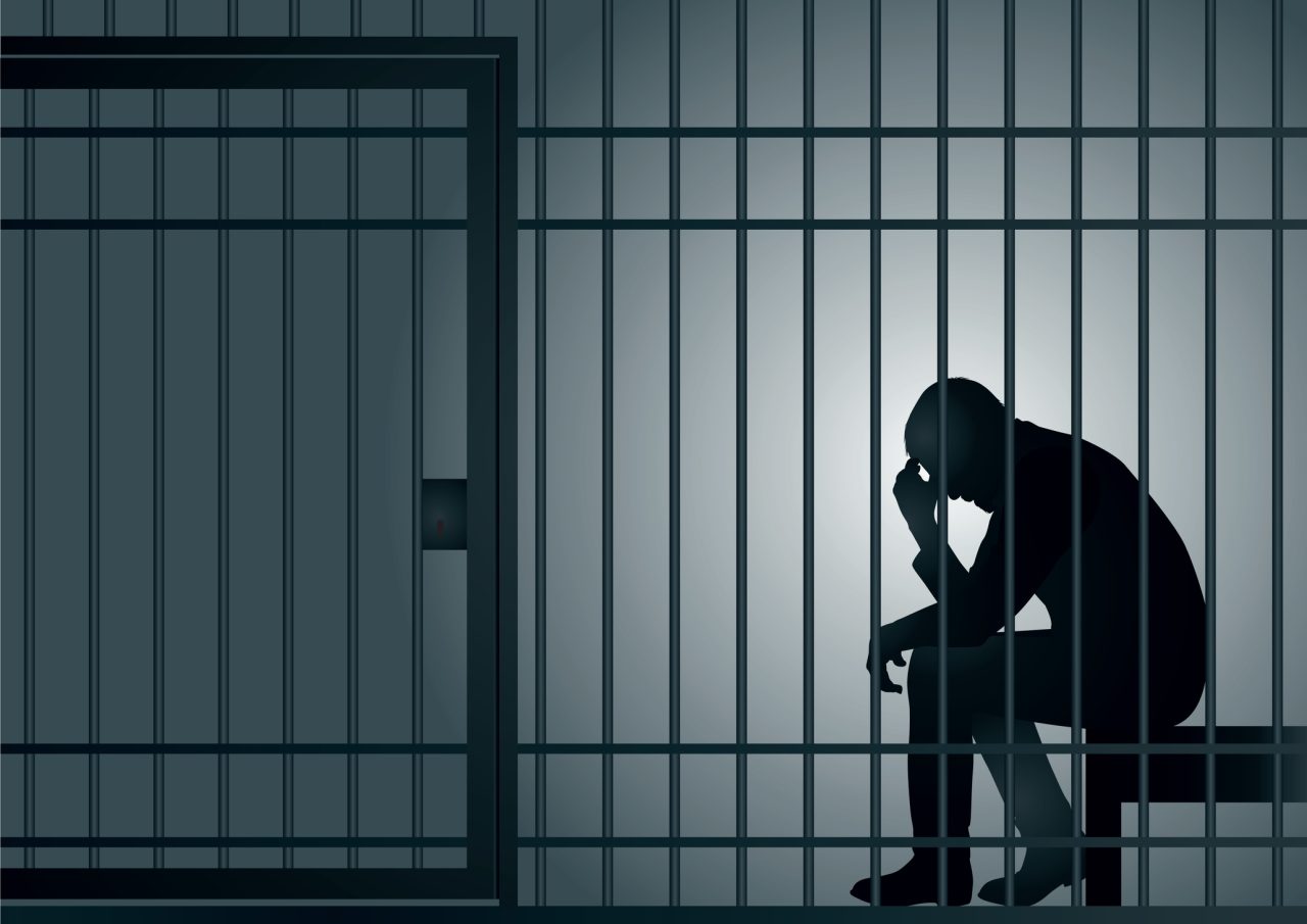 En mann sitter med hodet bøyd i en fengselscelle.