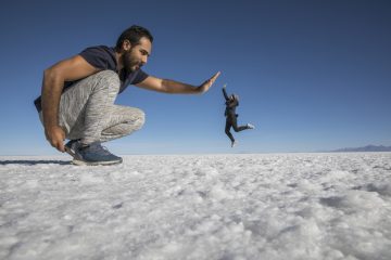 Mann sitter på huk foran i bildet. Kvinne står langt unna. Det ser ut som hun er mye mindre enn mannen.