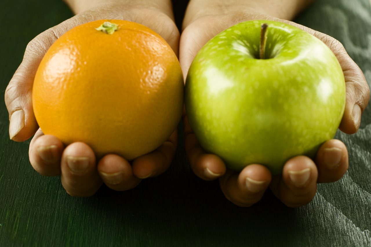 En person holder frem et eple og en appelsin.