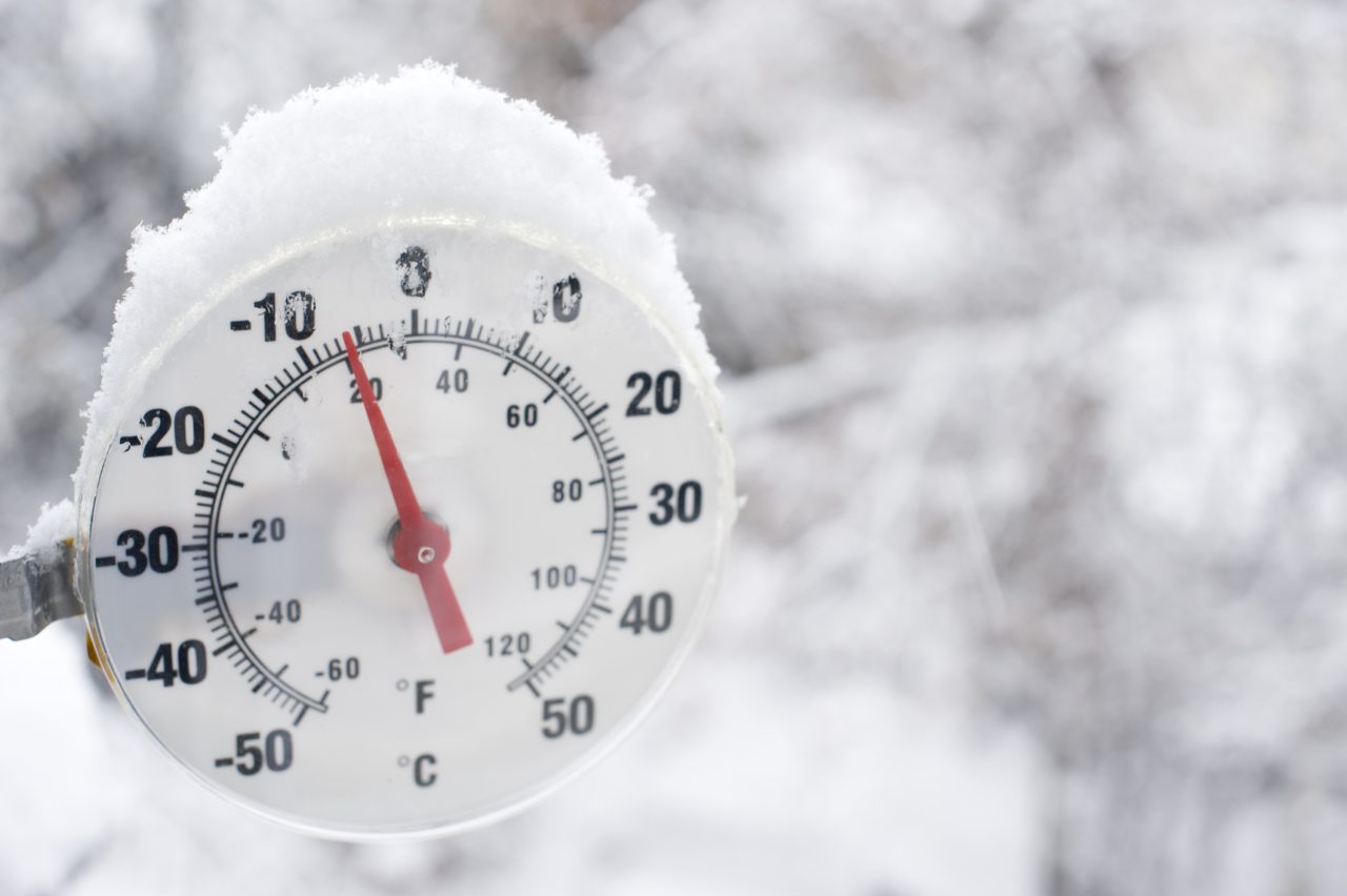 Frossen rund gradestokk med rød pil og snø på toppen.