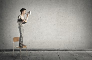 Ung gutt står på en stol og roper i en megafon.