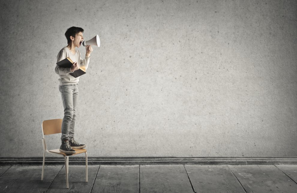 Ung gutt står på en stol og roper i en megafon.