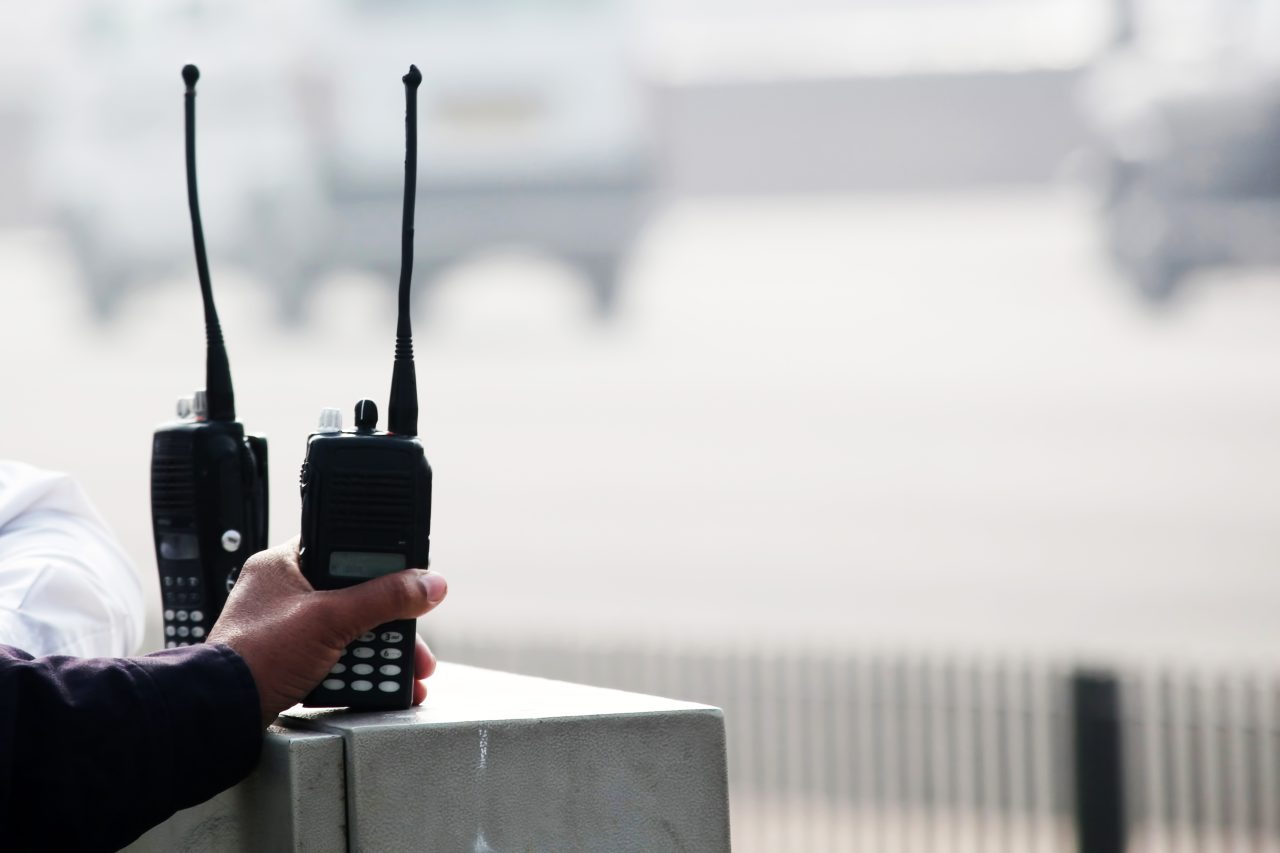 En person griper tak i en av to walkie-talkier som står på et bord.