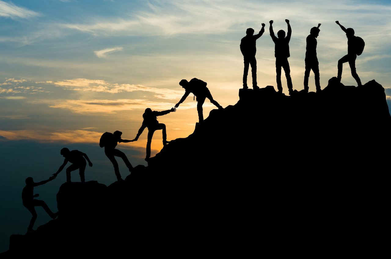 En gruppe mennesker hjelper hverandre opp på en fjelltopp.