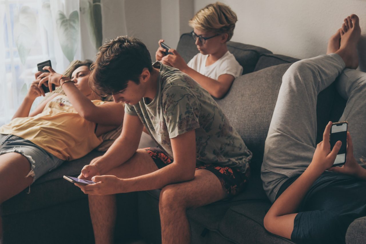 Unge gutter sitter henslengt i en sofa og ser på hver sin mobilskjerm.