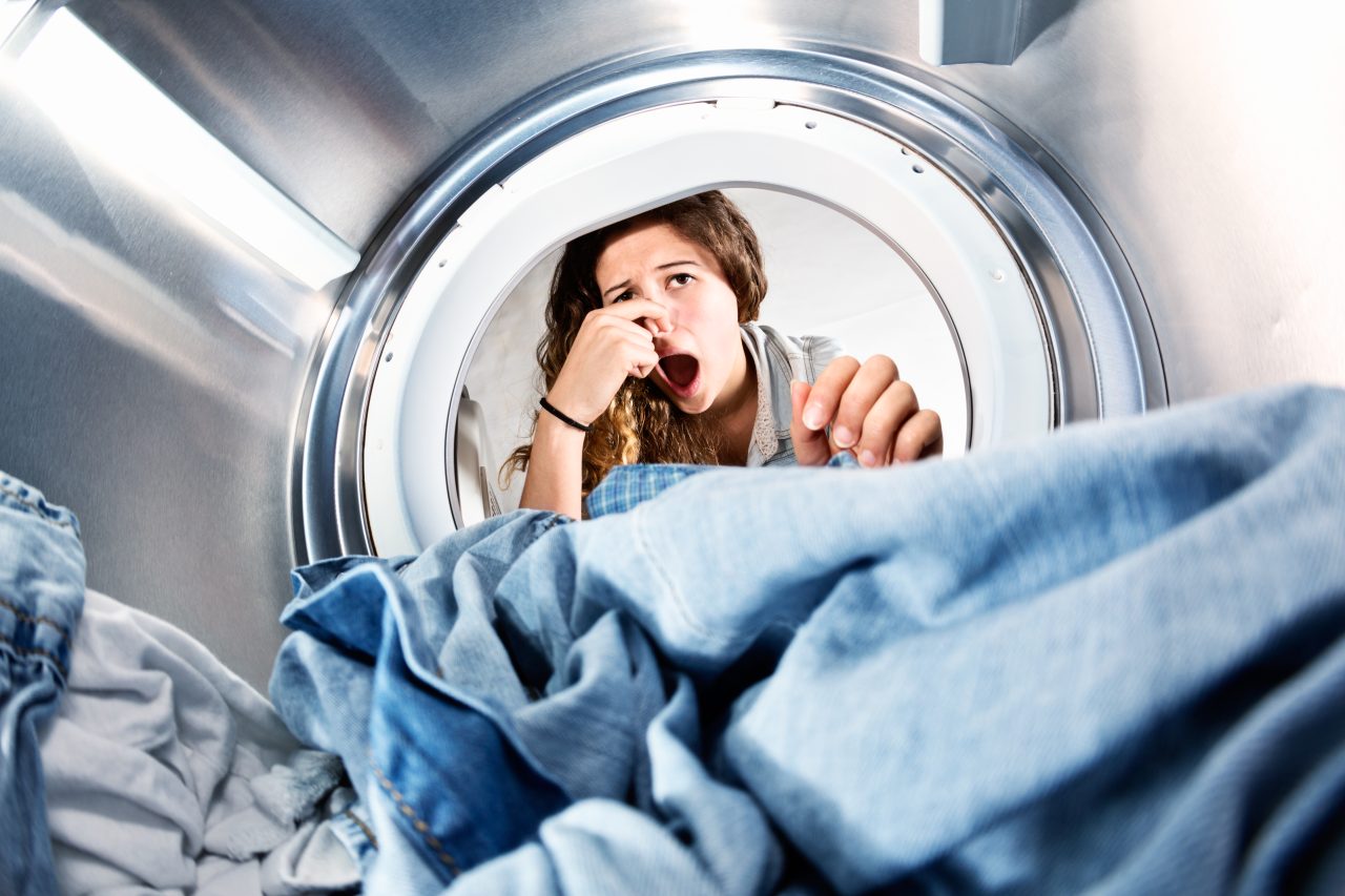 Voksen dame som ser inn i en vaskemaskin og holder seg for nesa.