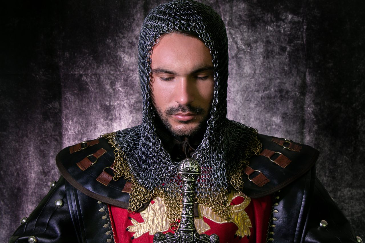 Portrett av en ridder med brynje på hodet, fargerik rustning og sverd.