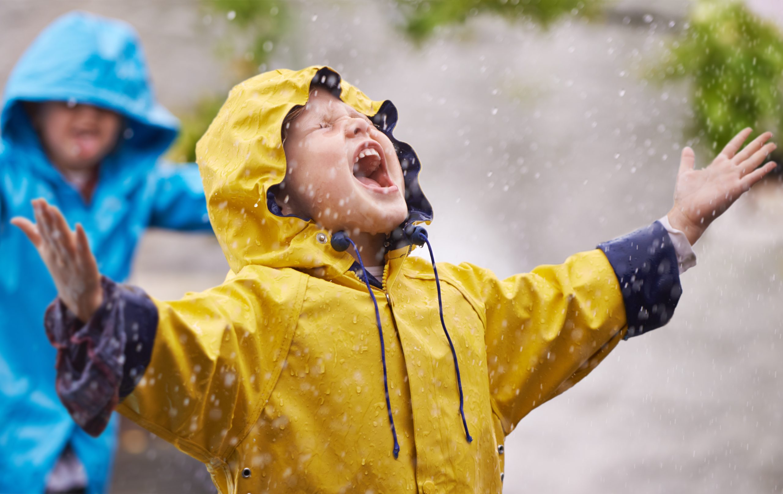 Ung gutt med gult regntøy står med armene rett ut og fanger regndråper med munnen.