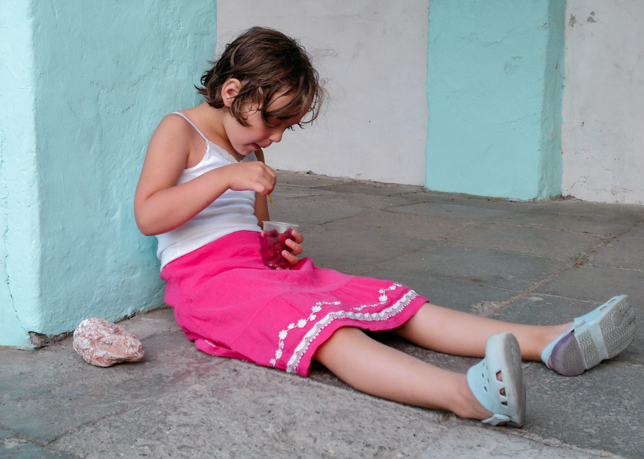 Jente sitter på bakken ved en vegg og spiser bringebær