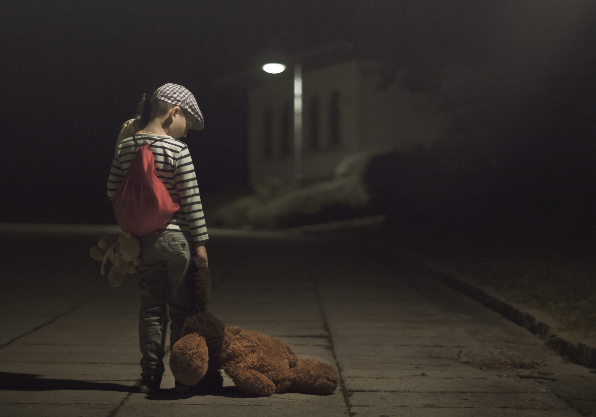 Barn alene i mørk gate med teddybjørn hengende fra hånden