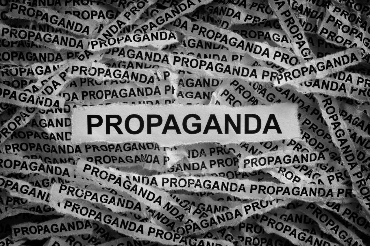 Ordet propaganda skrevet med sort tekst mange ganger på hvite papirstrimler.