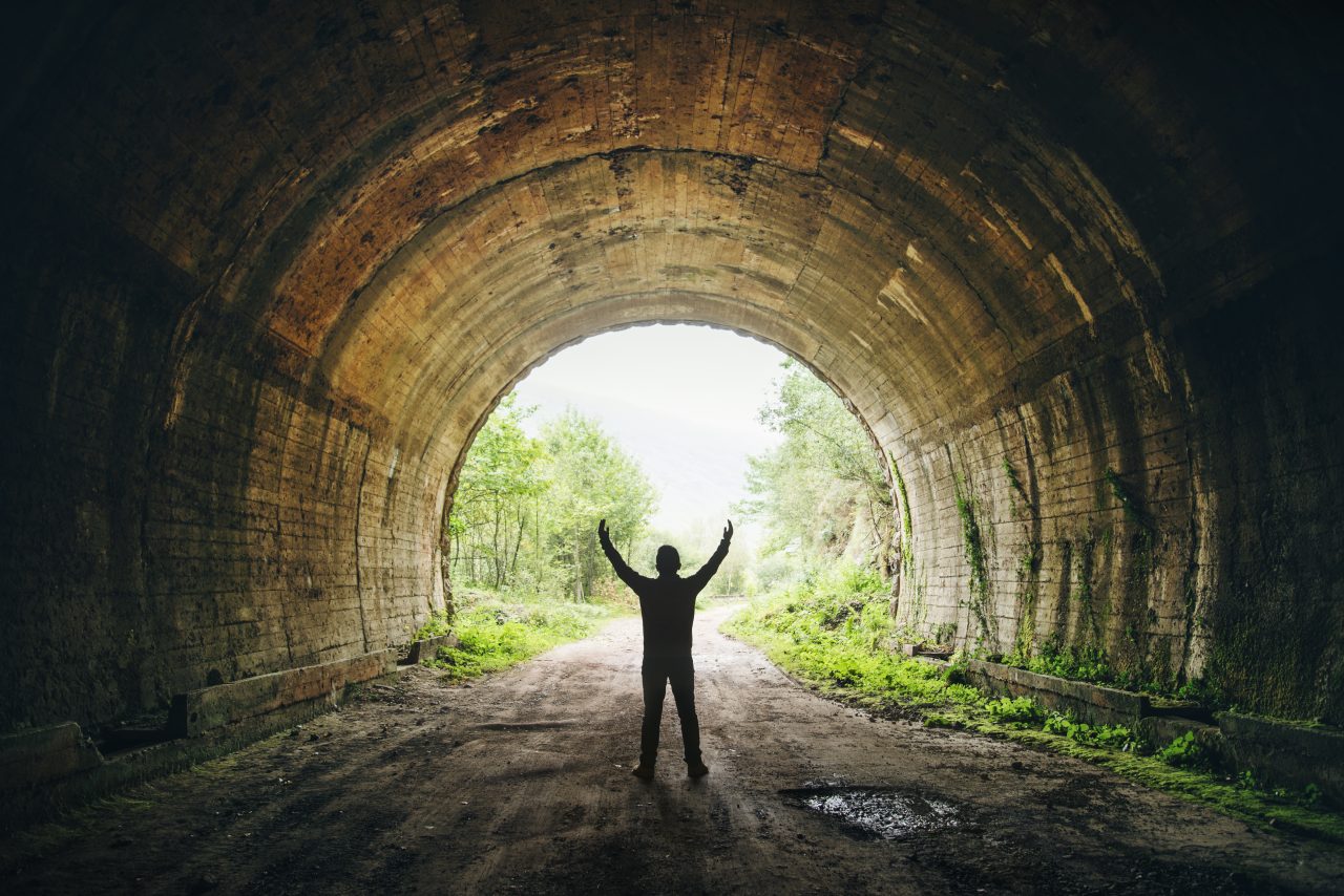 Person står med armene strukket i været ved åpningen av en tunnel med grønne trær på utsiden.