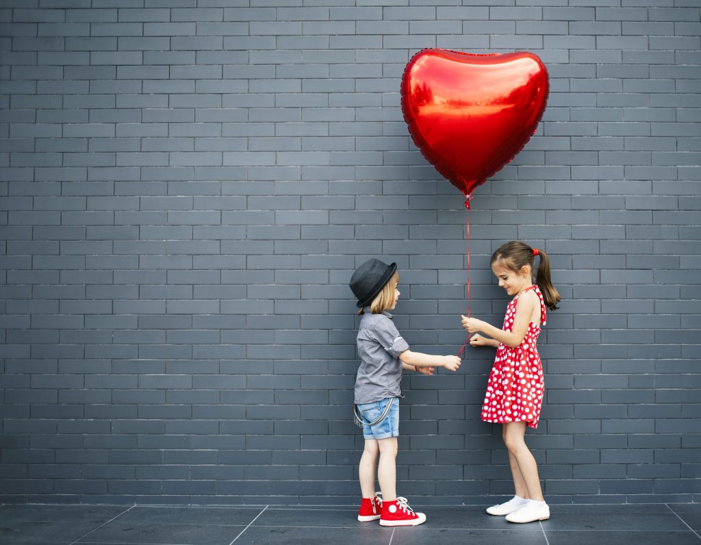 To barn som står mot en vegg med en hjerte ballong