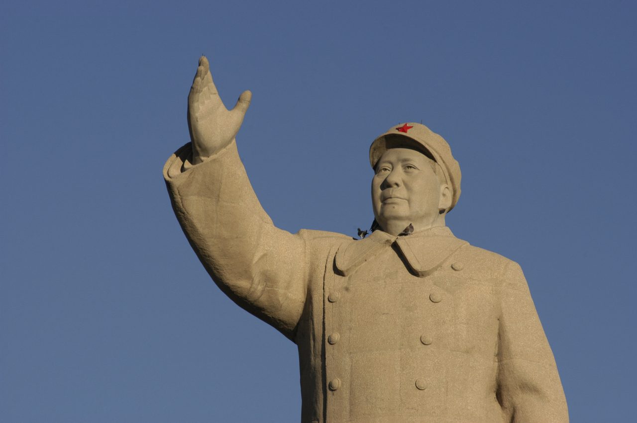 Statue av Mao Zedong der han løfter høyre arm opp mot den blå himmelen.