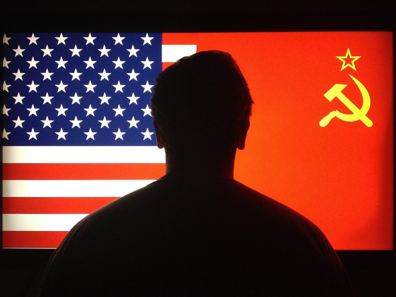 En sort silhouette står med ryggen til oss og ser på et amerikansk og et sovjetisk flagg.