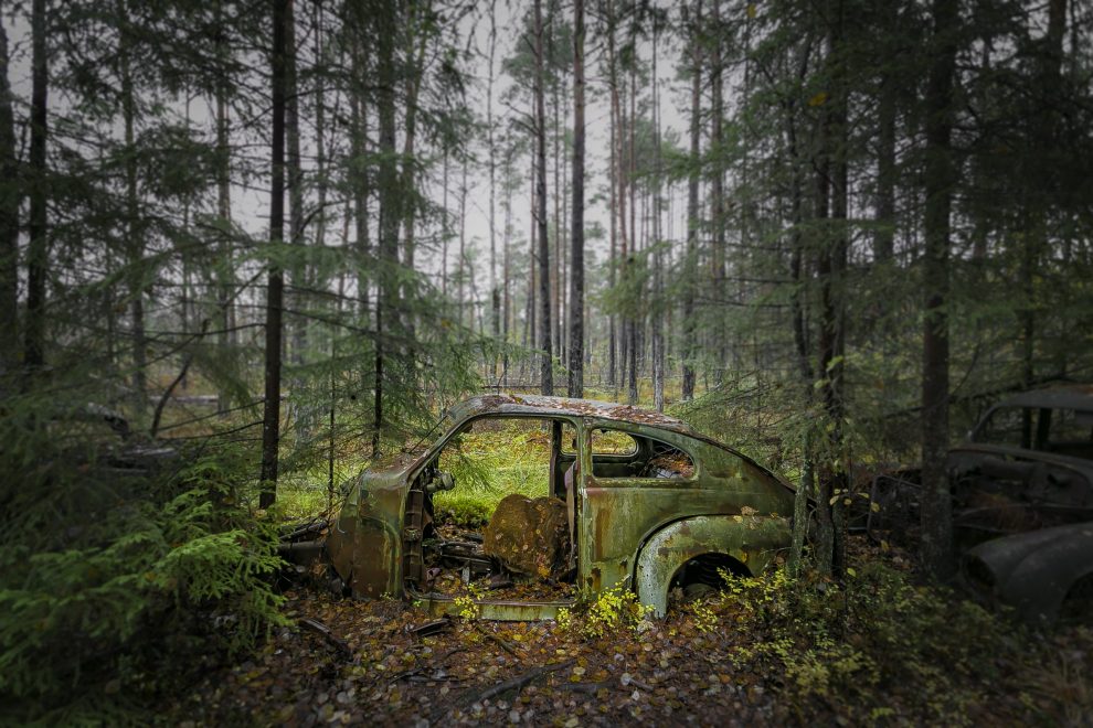 Bil som står og ruster bort i skogen.