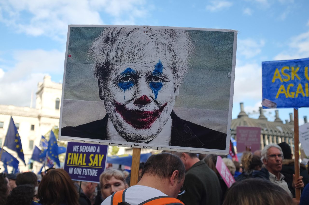 Folketog under demonstrasjon. Svær plakat av Boris Johnson med Jokeren-sminke manipulert inn.