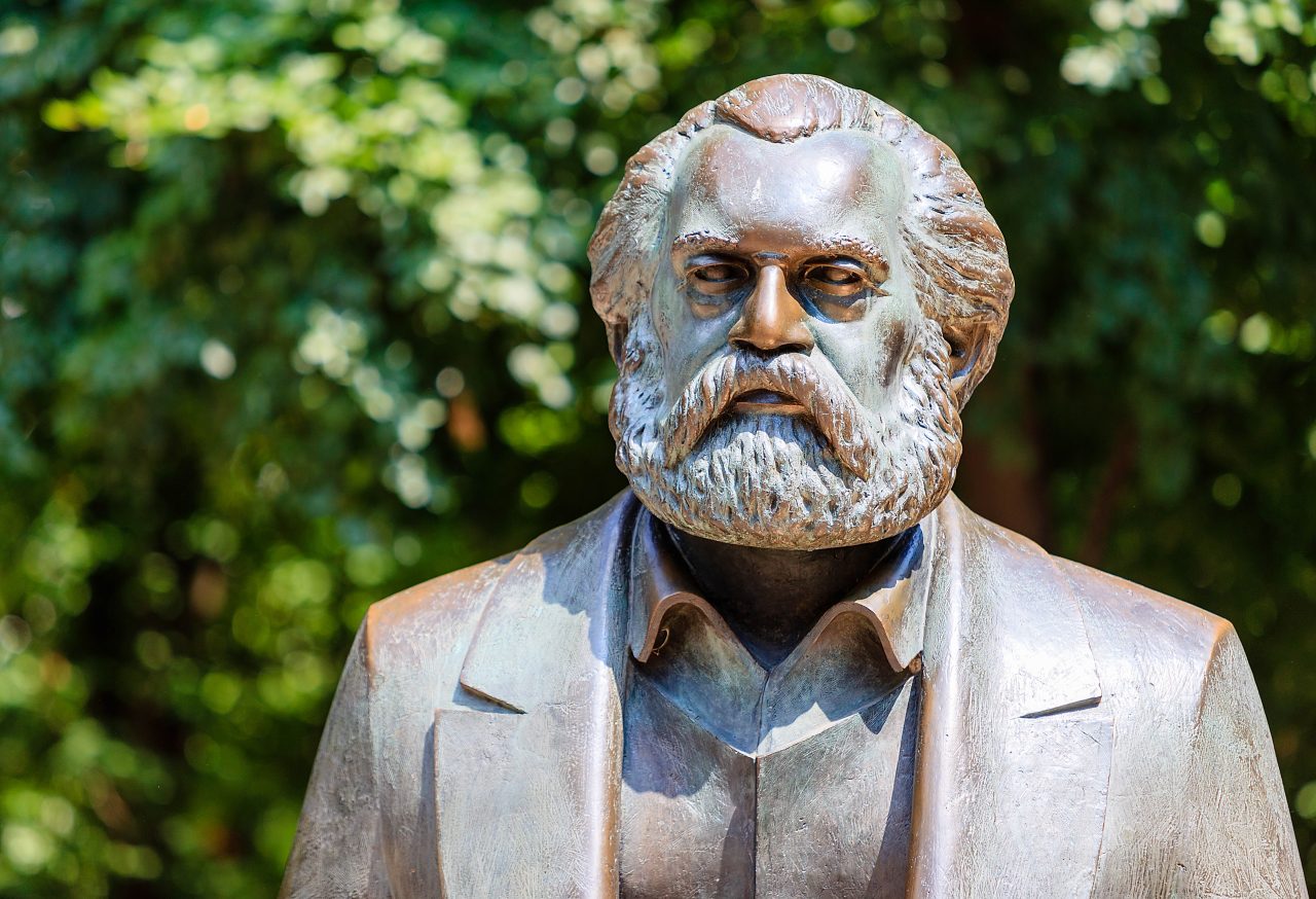 Bronsestatue av Karl Marx foran grønne løvtrær.