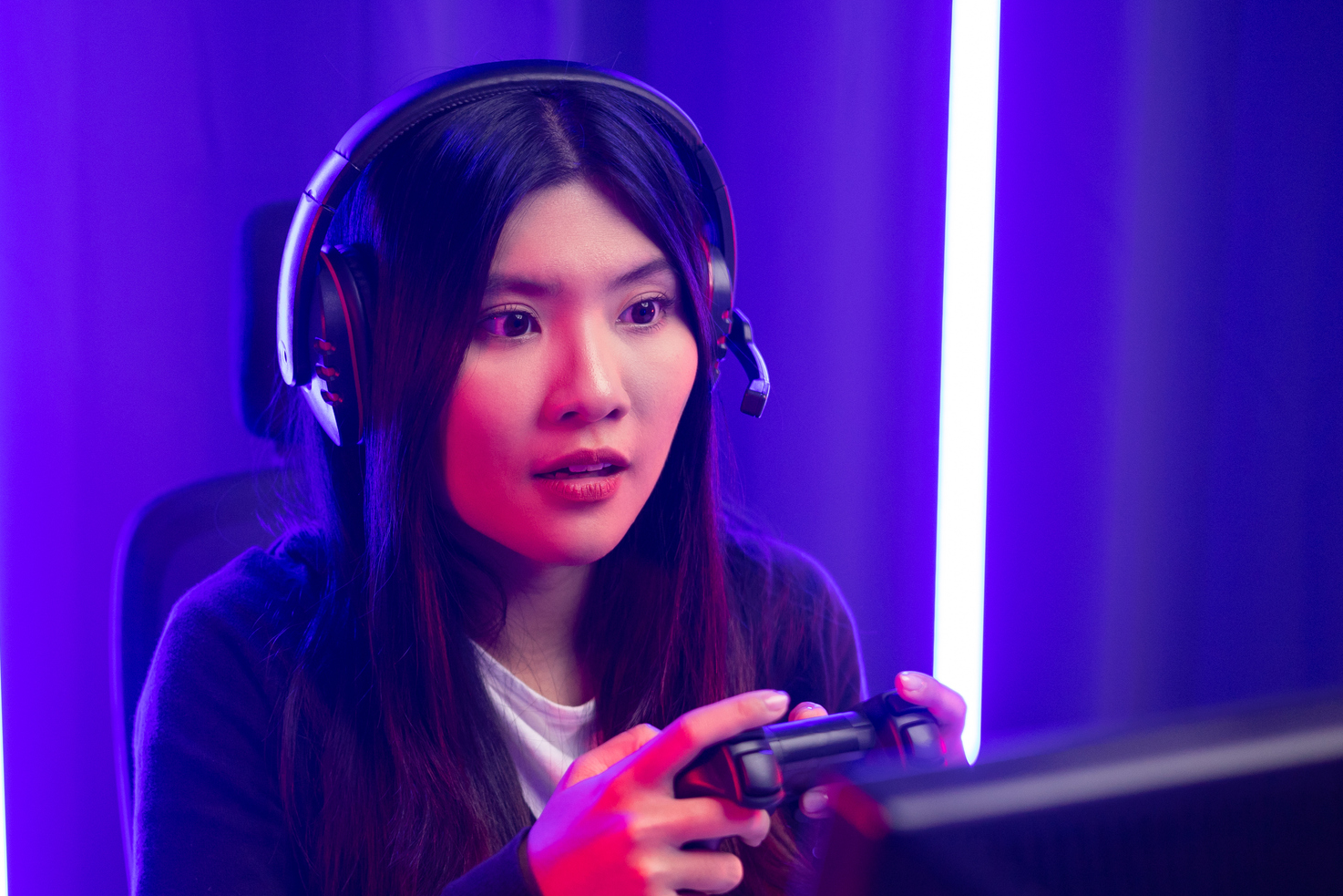 Kvinnelig streamer som spiller videospill foran en skjer med lilla og blå lys i bakgrunn.