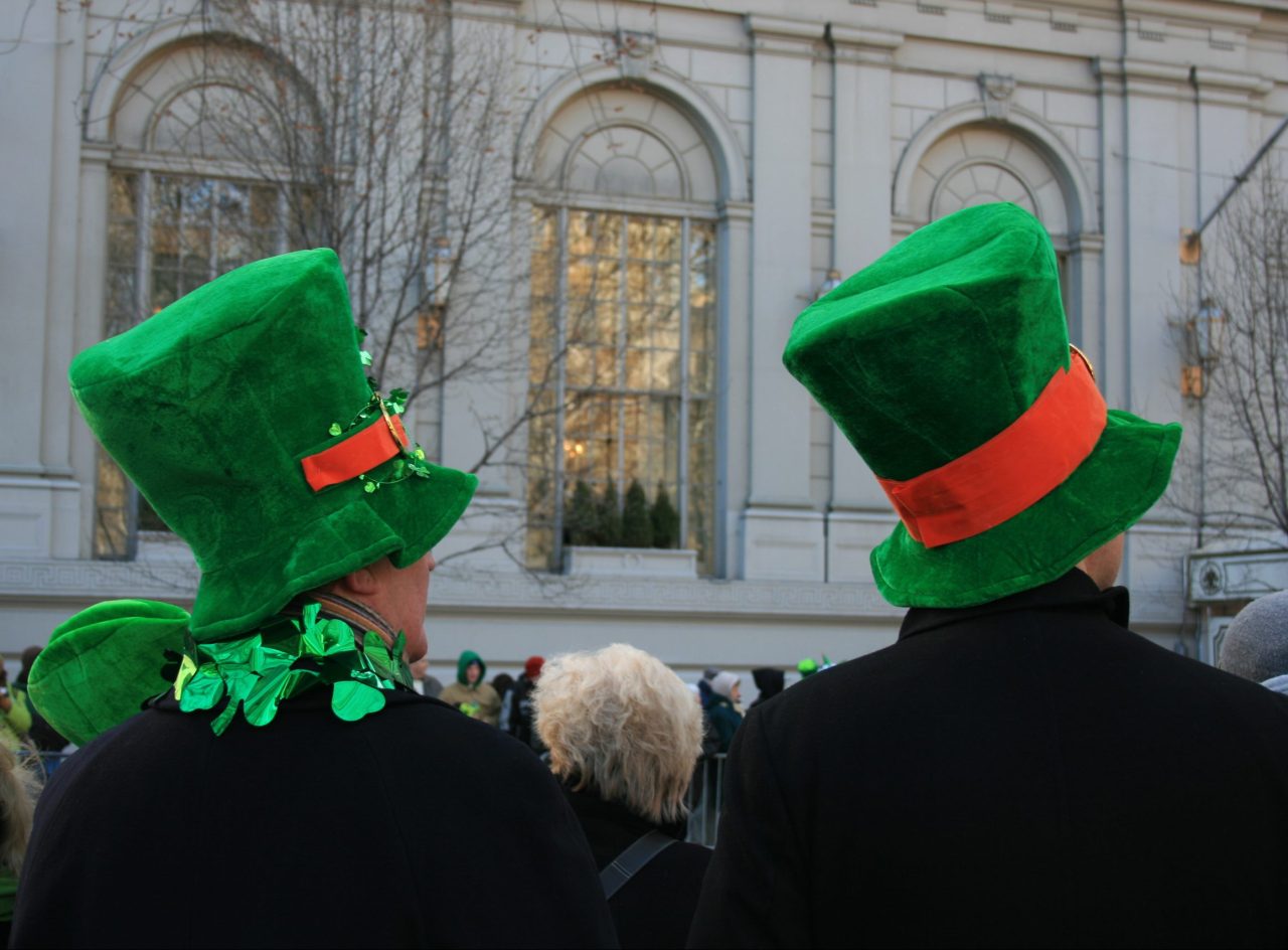 To menn med høye grønne hatter står og ser på en parade på Manhatten.