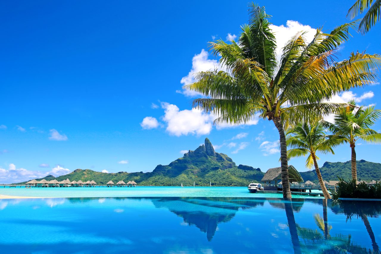 Bora Bora med palmetrær, blå himmel og blått hav.