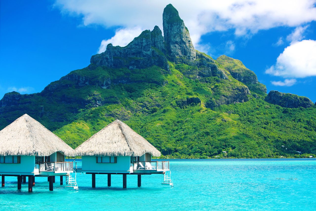 Bungalower i blått hav og et høyt frodig fjell på Tahiti.