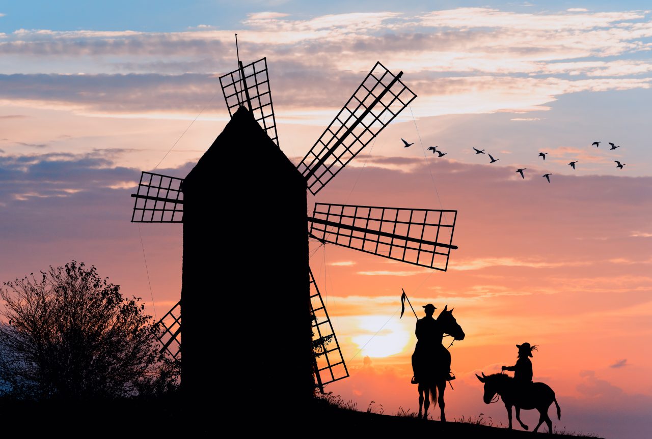 Don Quijote på hest og Sancho Panza på esel stående ved siden av en vindmølle i solnedgang.