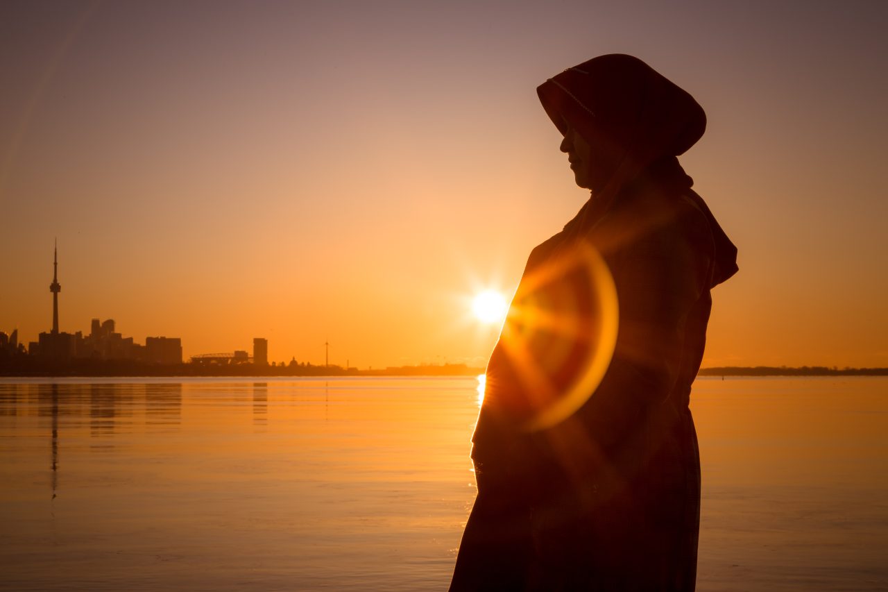 En gravid muslimsk kvinne poserer foran solnedgangen