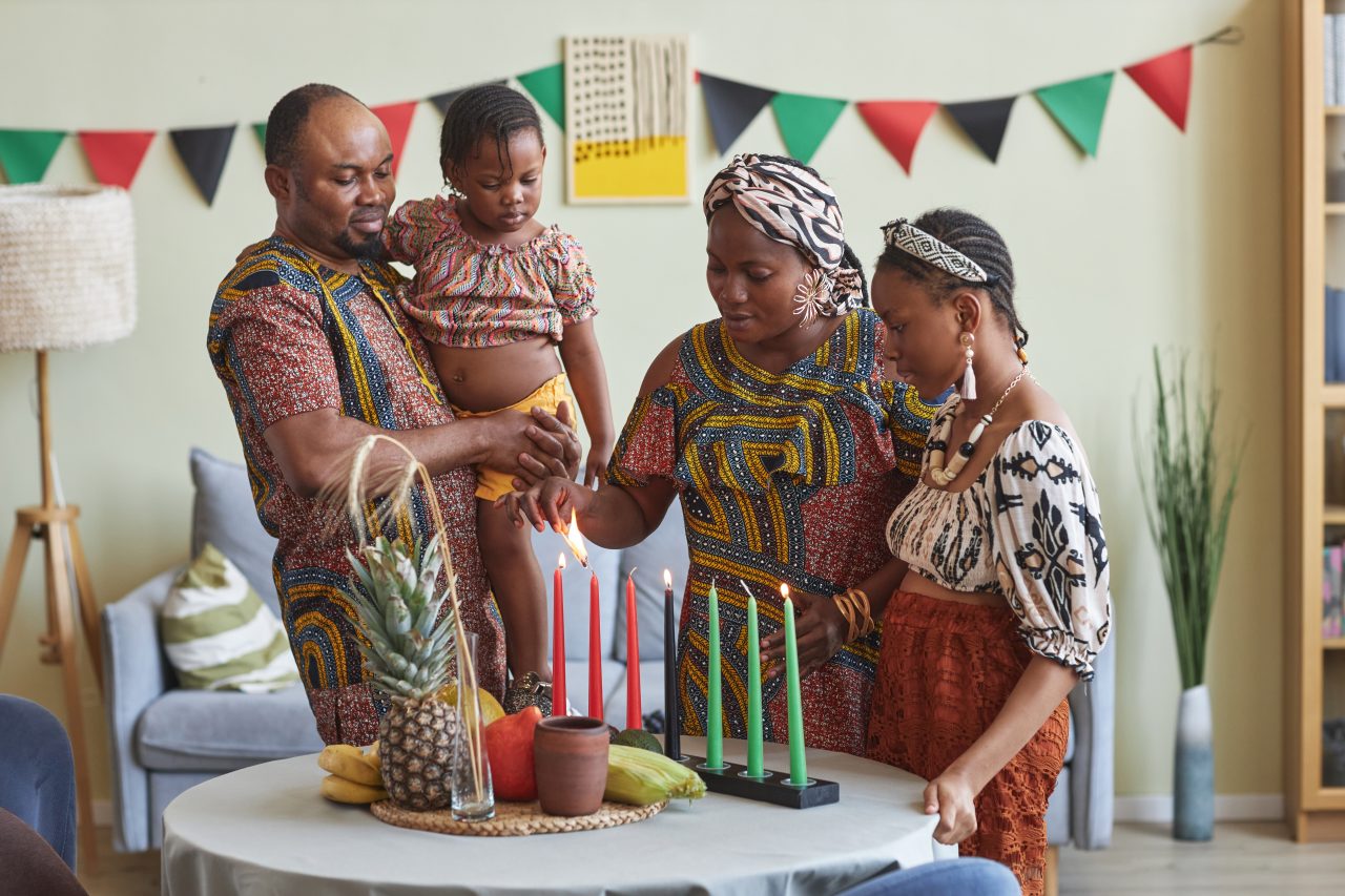 Afrikansk familie med to voksne og to barn feirer Kwanzaa og tenner syvarmet lysestake med røde og grønne lys.