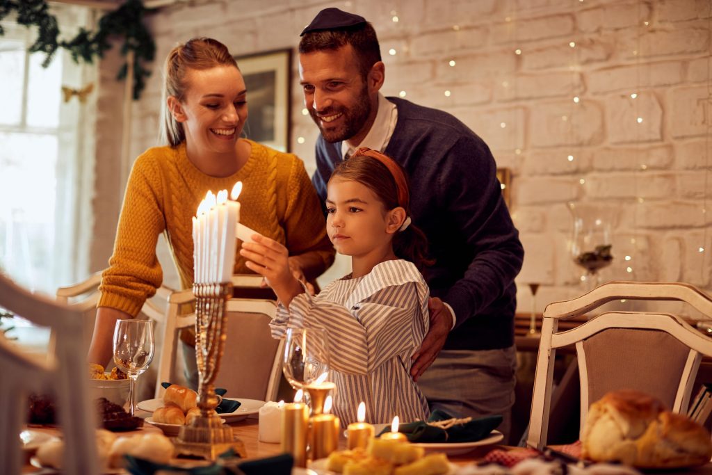 Jødisk familie med mor, far og datter tenner en åttearmet lysestake som står på et festpyntet bord.