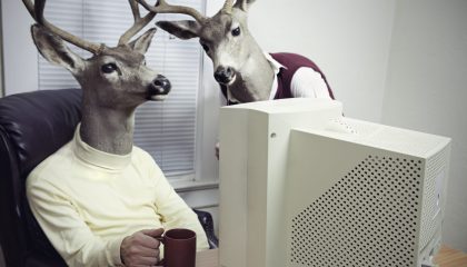 To menneskefigurer med hjortehoder sitter foran PC og ser på noe sammen.