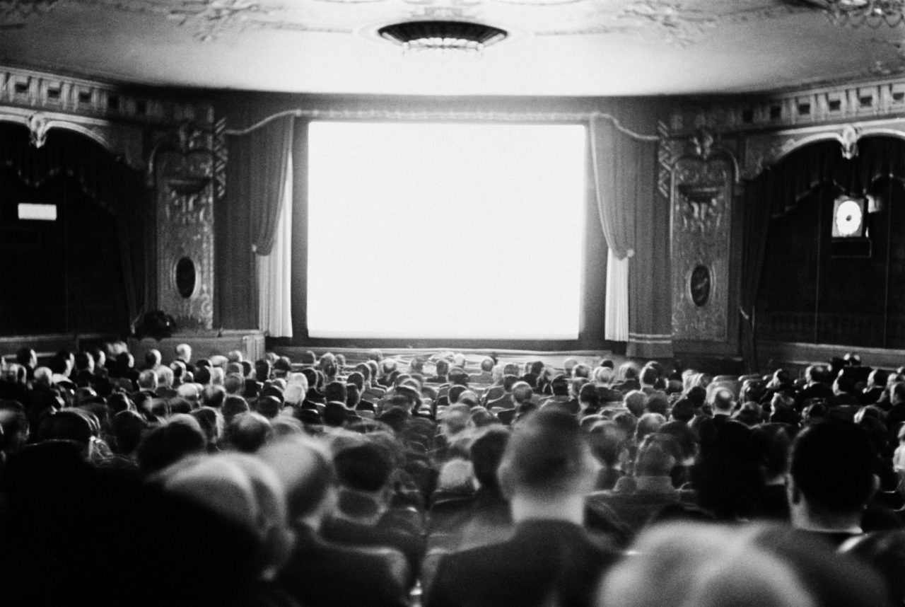 Publikum som ser mot et lerret i en kinosal fra 1935