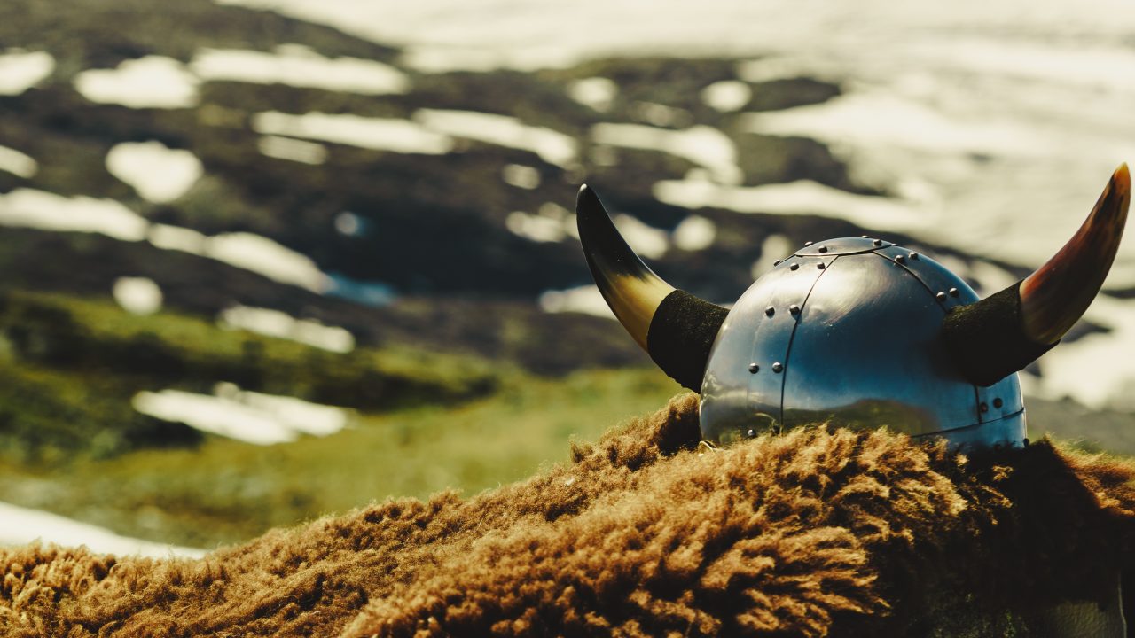 Vikinghjelm som ligger på en brun pels med fjell i bakgrunnen