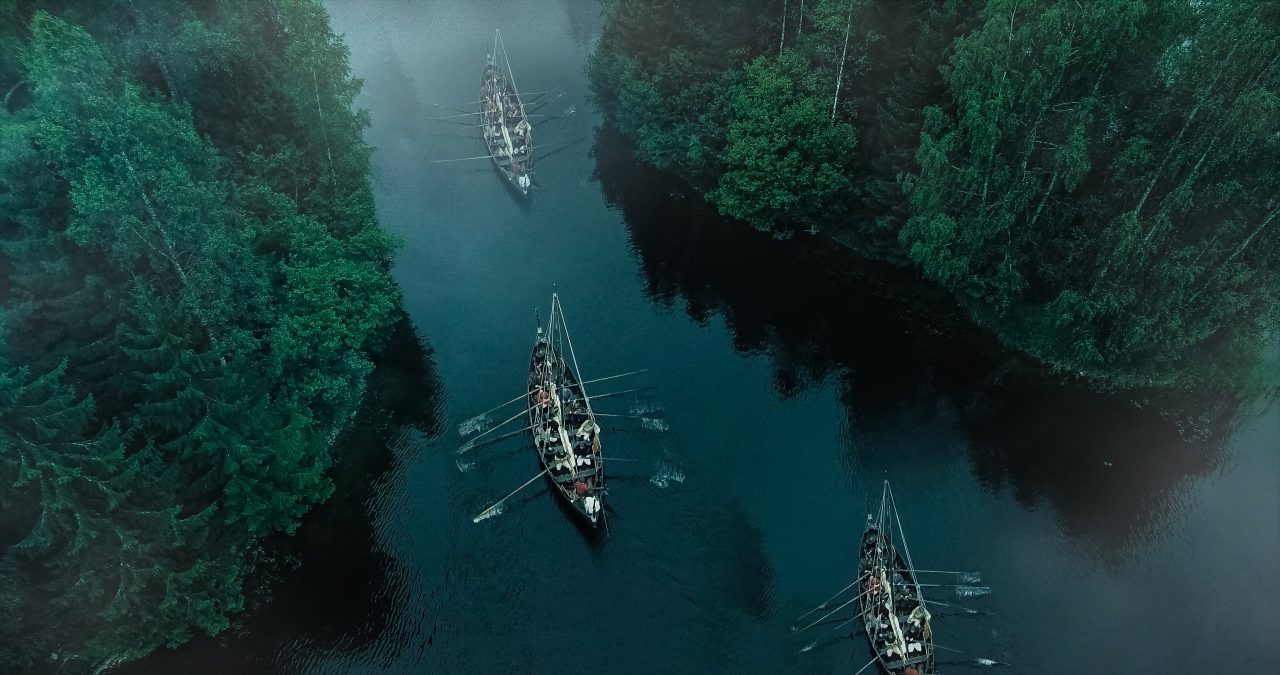 Tre vikingskip i en fjord sett fra luften