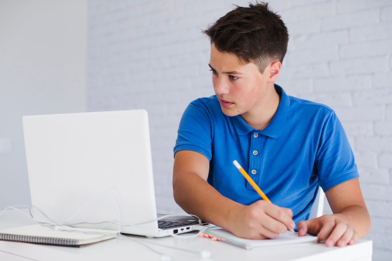 Tenåring sitter foran en pc mens han noterer i en skrivebok