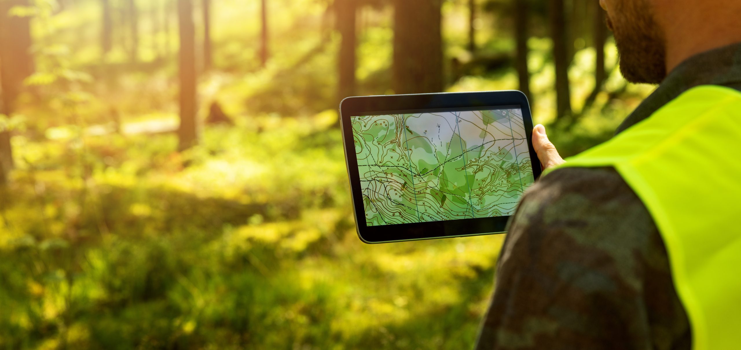Mann som arbeider med topografiske kartdata på digitalt nettbrett i skogen. Banner med kopiplass