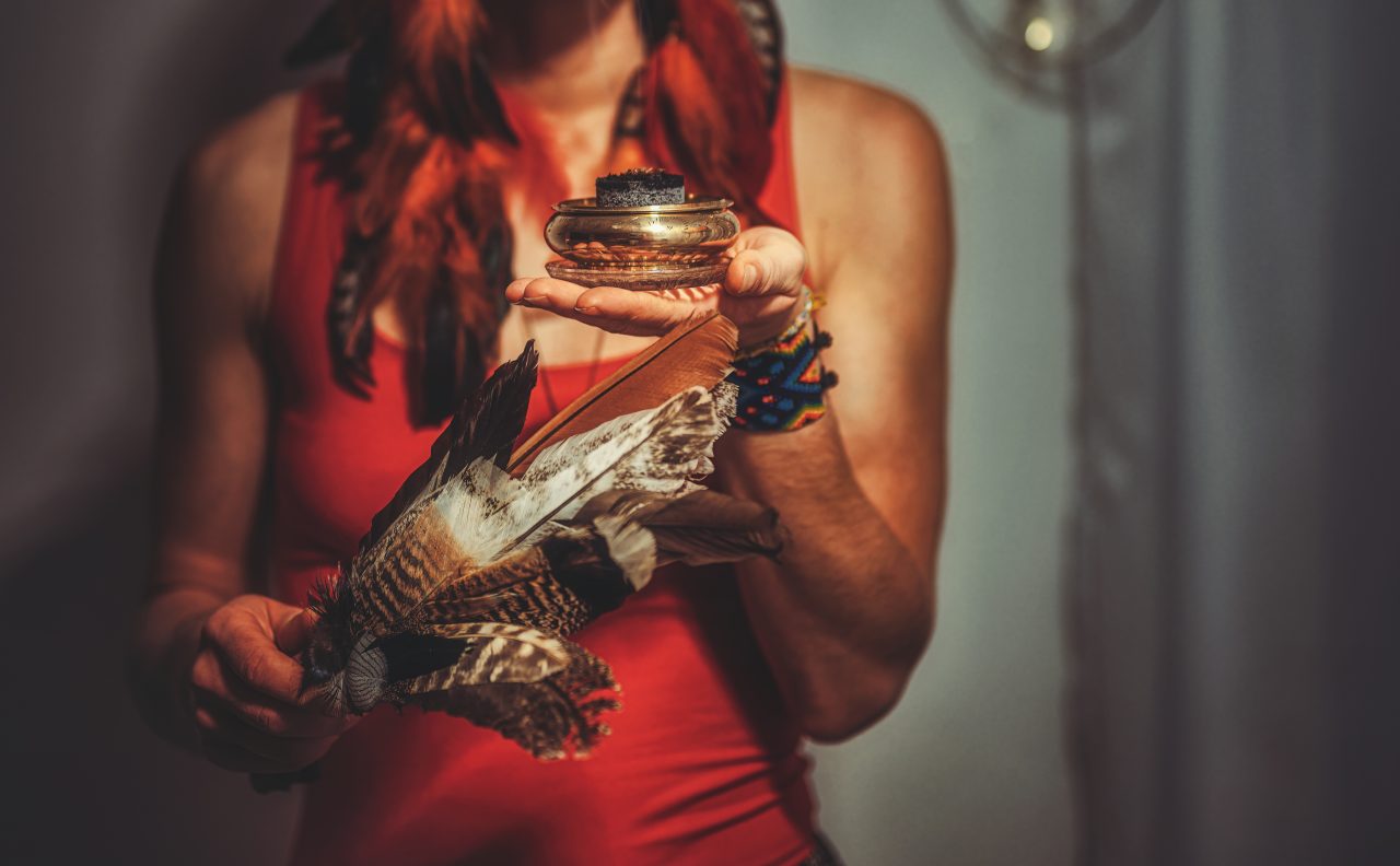 En kvinnelig sjaman med fjær i en hånd og en krukke i den andre.