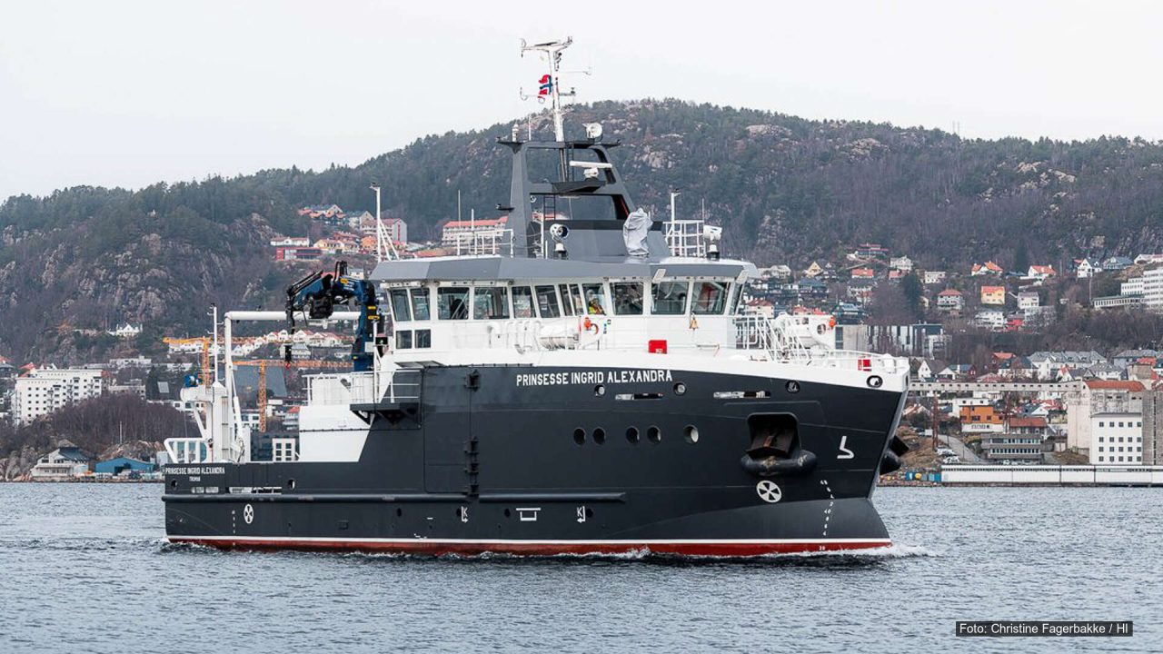 Forskningsfartøyet Prinsesse Ingrid Alexandra seiler i Byfjorden med by og fjell i bakgrunnen.