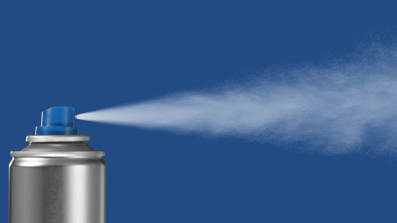 Sprayboks som sprayer en sky av fin væske ut i luften mot høyre, på blå bakgrunn.