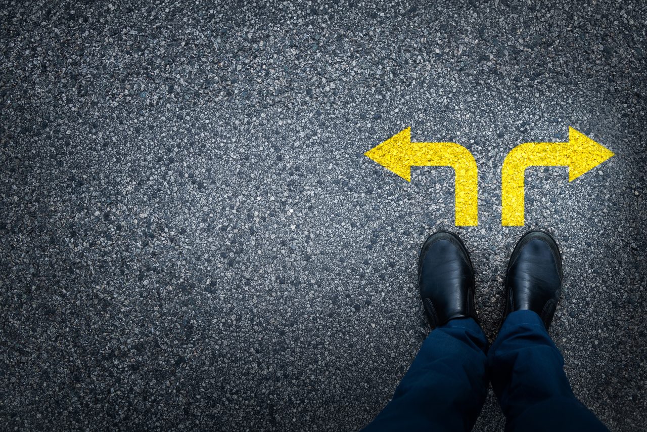 Person står på asfalt foran to gule piler som peker i motsatte retninger