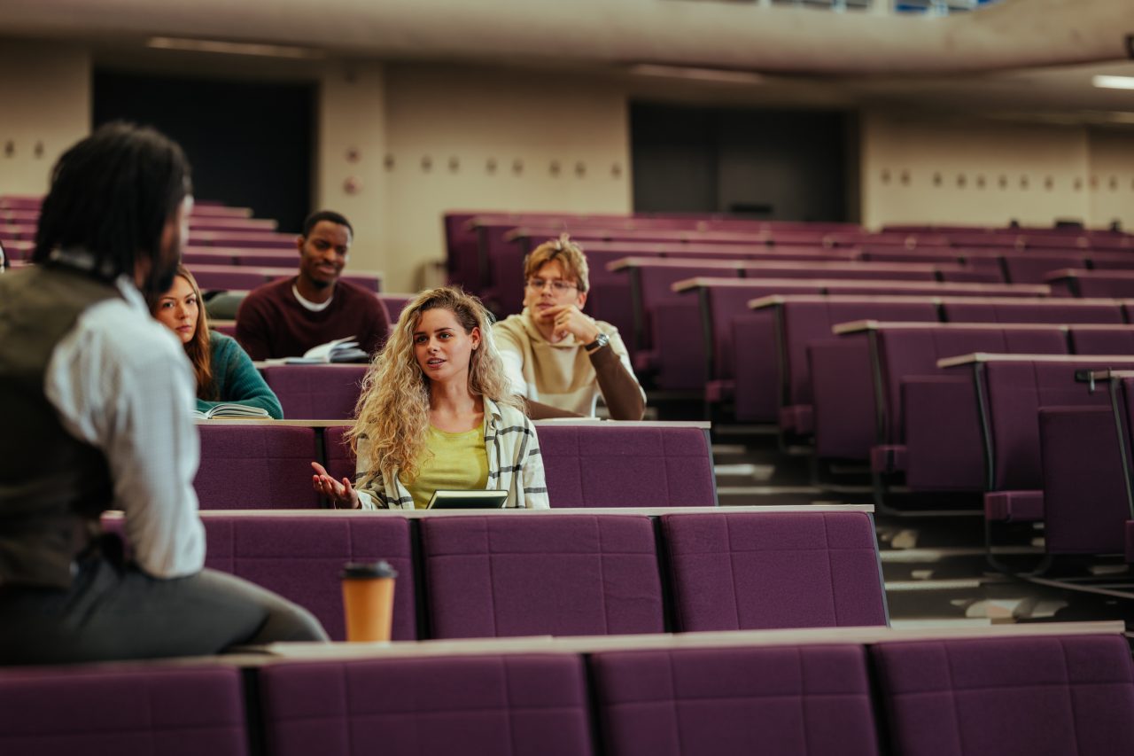 En universitetsstudent stiller et spørsmål under en forelesning i et klasserom