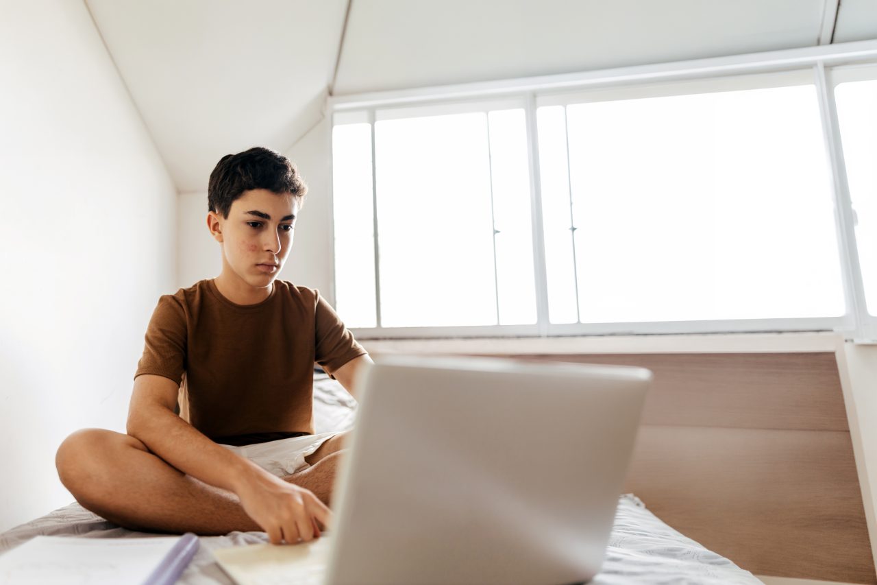 Tenåring som sitter på sengen med en bærbar PC